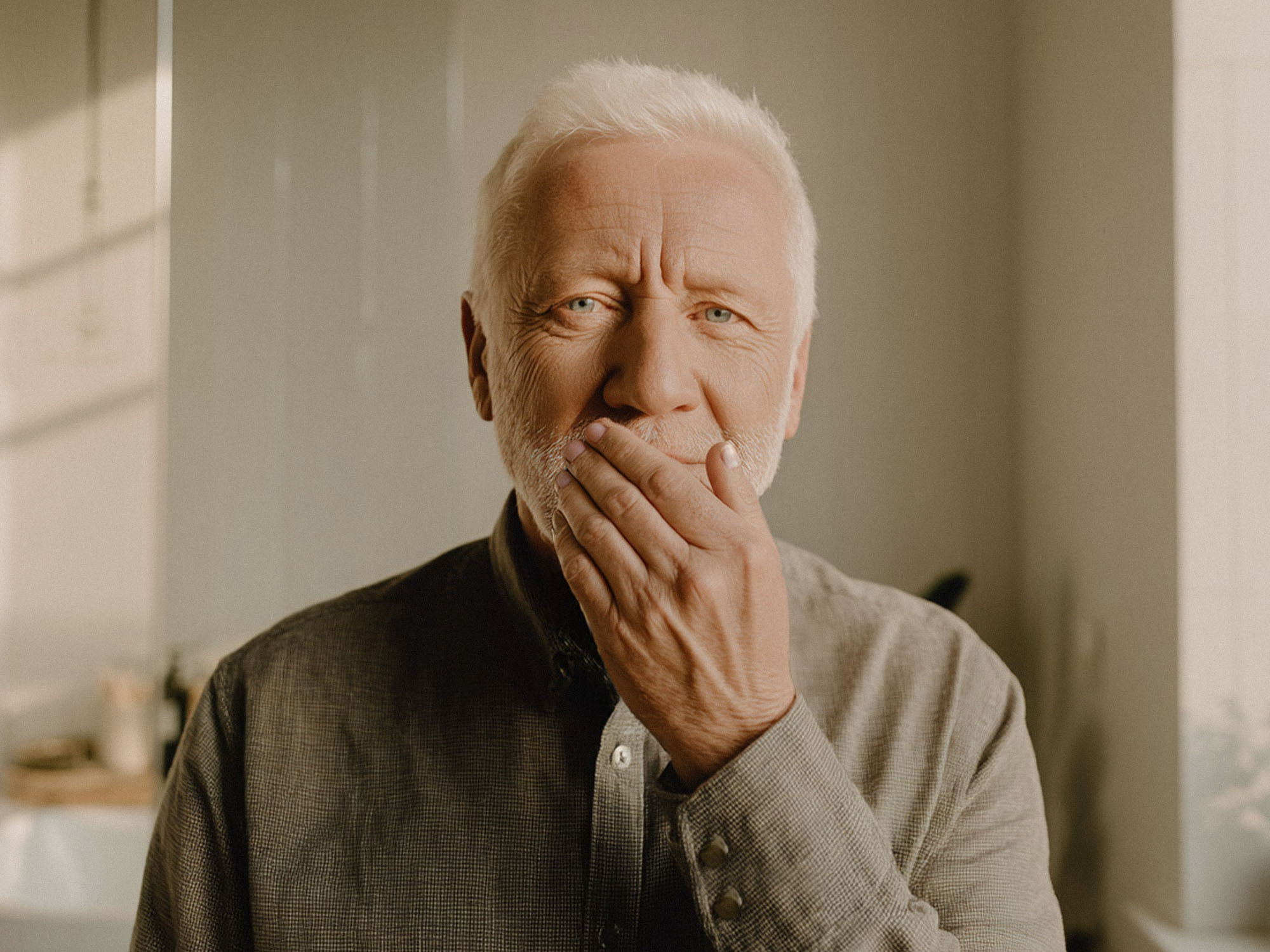 Älterer Mann hält die Hand vor den Mund